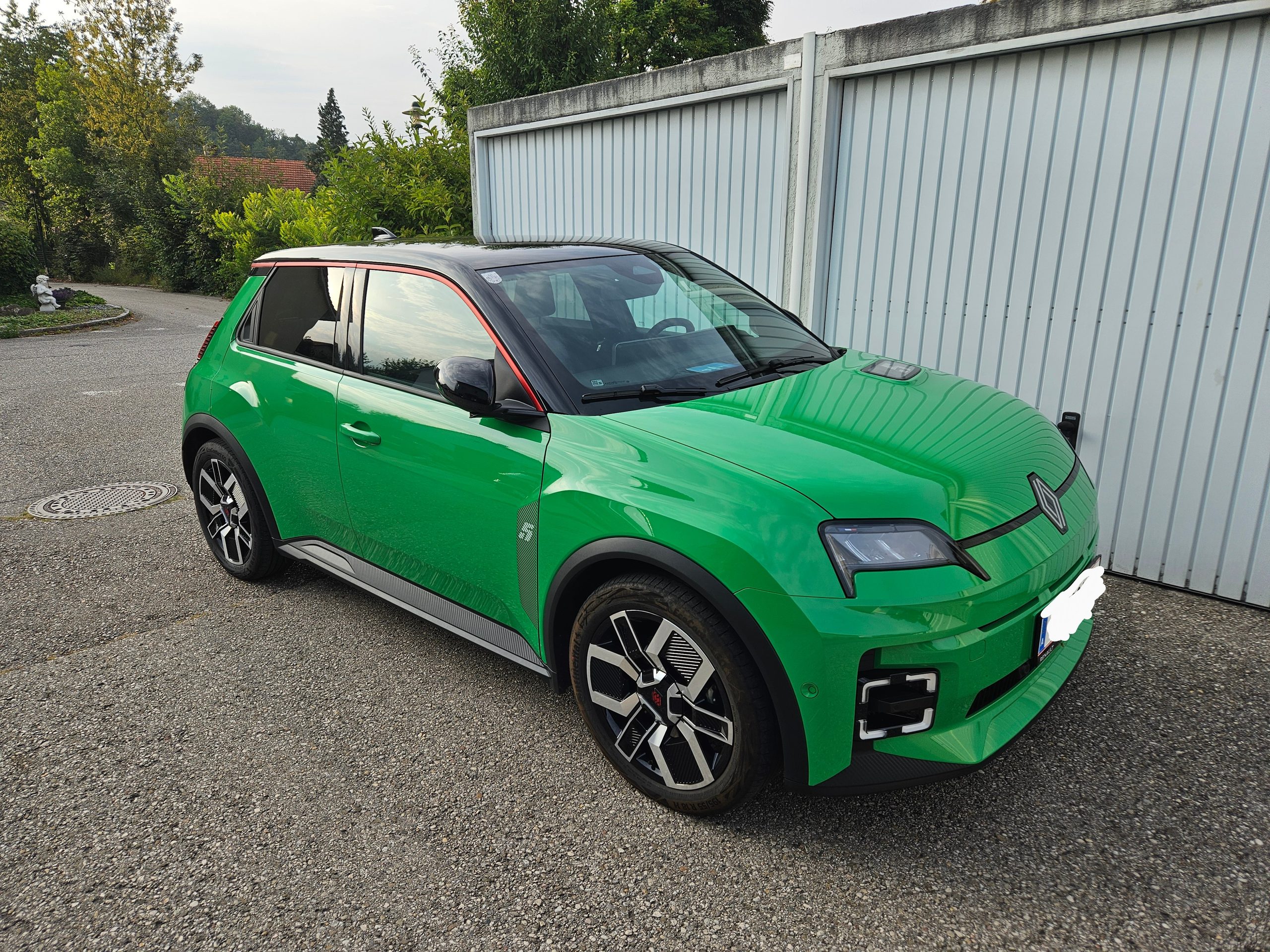 Ein grüner Renault 5 e-Tech (EV) mit schwarzem Dach vor einer Doppelgarage